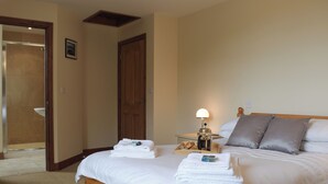A hotel room with a bed, a bedside table with a lamp, a wooden bench, and a door leading to a bathroom. - 3 bedroom accommodation in Llangennith, near Swansea (Llangennith, near Swansea)