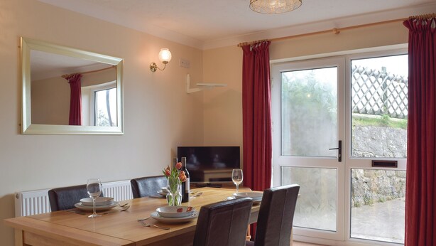A dining area with a wooden table, chairs, a television, and a view through a glass door. - 3 bedroom accommodation in Llangennith, near Swansea (Llangennith, near Swansea)
