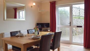 A dining area with a wooden table, chairs, a television, and a view through a glass door.