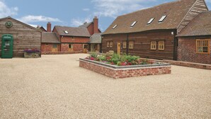 Un patio con suelo de grava, edificios de madera con detalles de ladrillo y un parterre floral.