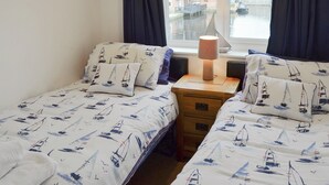 A bedroom with two beds, a nightstand, and a window with curtains.