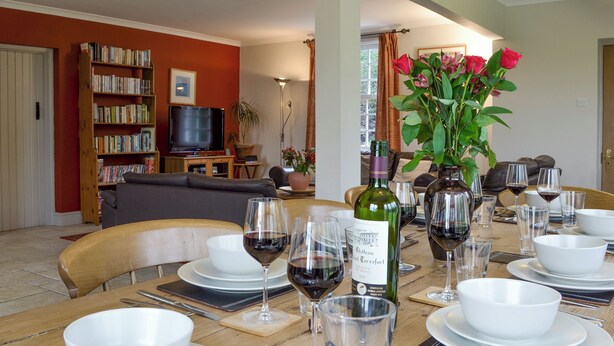 A dining area with a table set for a meal, surrounded by bookshelves and a television. - 4 bedroom accommodation in Pett (Pett)