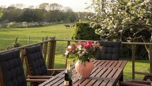 A wooden table with a bottle of champagne and a glass, surrounded by cushioned chairs. - 4 bedroom accommodation in Pett (Pett)