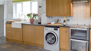 A modern kitchen with wooden cabinets, a built-in washing machine, and a stainless steel oven. - 4 bedroom accommodation in Pett (Pett)