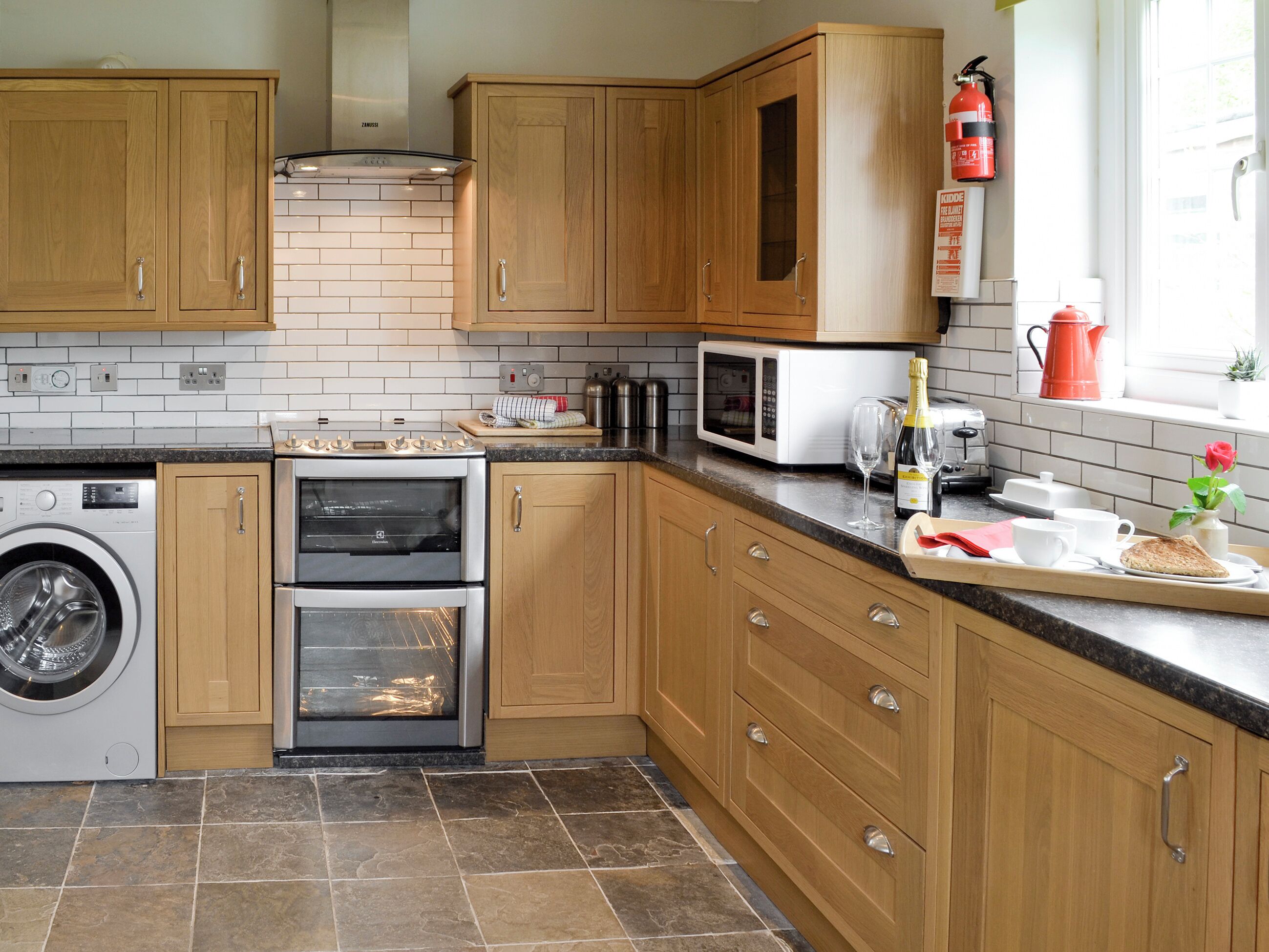 A modern kitchen with wooden cabinets, a built-in oven, a microwave, and a washing machine.