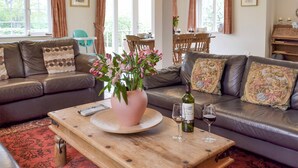 A living room with a brown leather sofa, a wooden coffee table, and a pink vase with flowers. There are two wine glasses and a bottle of wine on the table. - 4 bedroom accommodation in Pett (Pett)