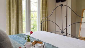 A neatly made bed with a tray of breakfast, including toast and a cup, in a room with a window and curtains. - 4 bedroom accommodation in Pett (Pett)