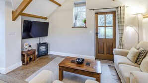 Un accogliente soggiorno con soffitto in legno, un televisore a schermo piatto, un caminetto, un tavolino in legno e un divano beige.