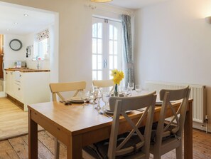 A dining area with a wooden table set for two, chairs, and a vase with yellow flowers. - 3 bedroom accommodation in Middleton, Freshwater (Middleton, Freshwater)