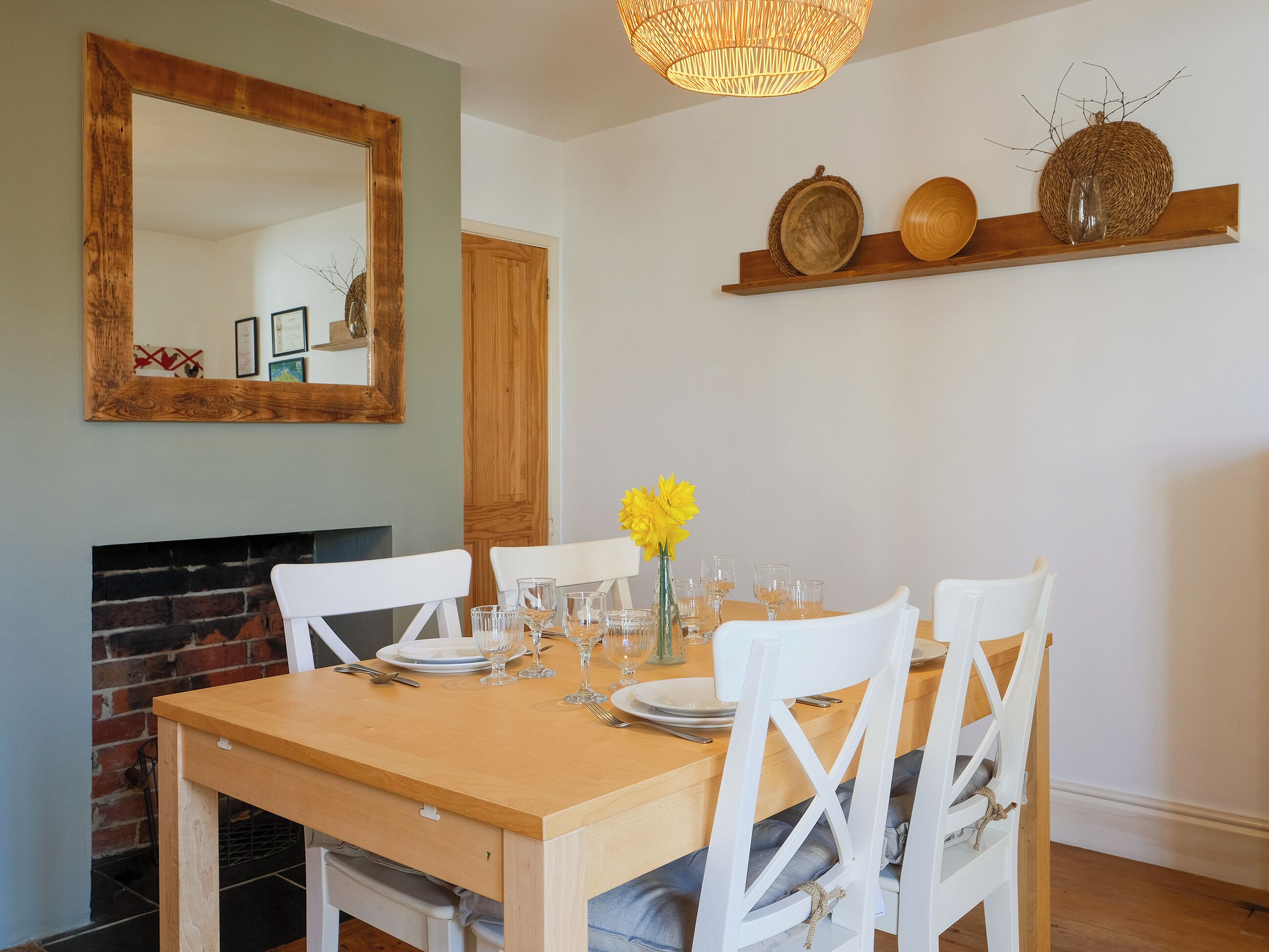 Un coin repas avec une table en bois, des chaises blanches, un miroir et une cheminée.