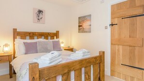 A neatly made bed with a wooden headboard, white linens, and a folded towel on the side. There are two bedside tables with lamps, a wooden door, and a wall with two framed pictures. - 3 bedroom accommodation in Ashford-in-the-Water, near Bakewell (Ashford-in-the-Water, near Bakewell)
