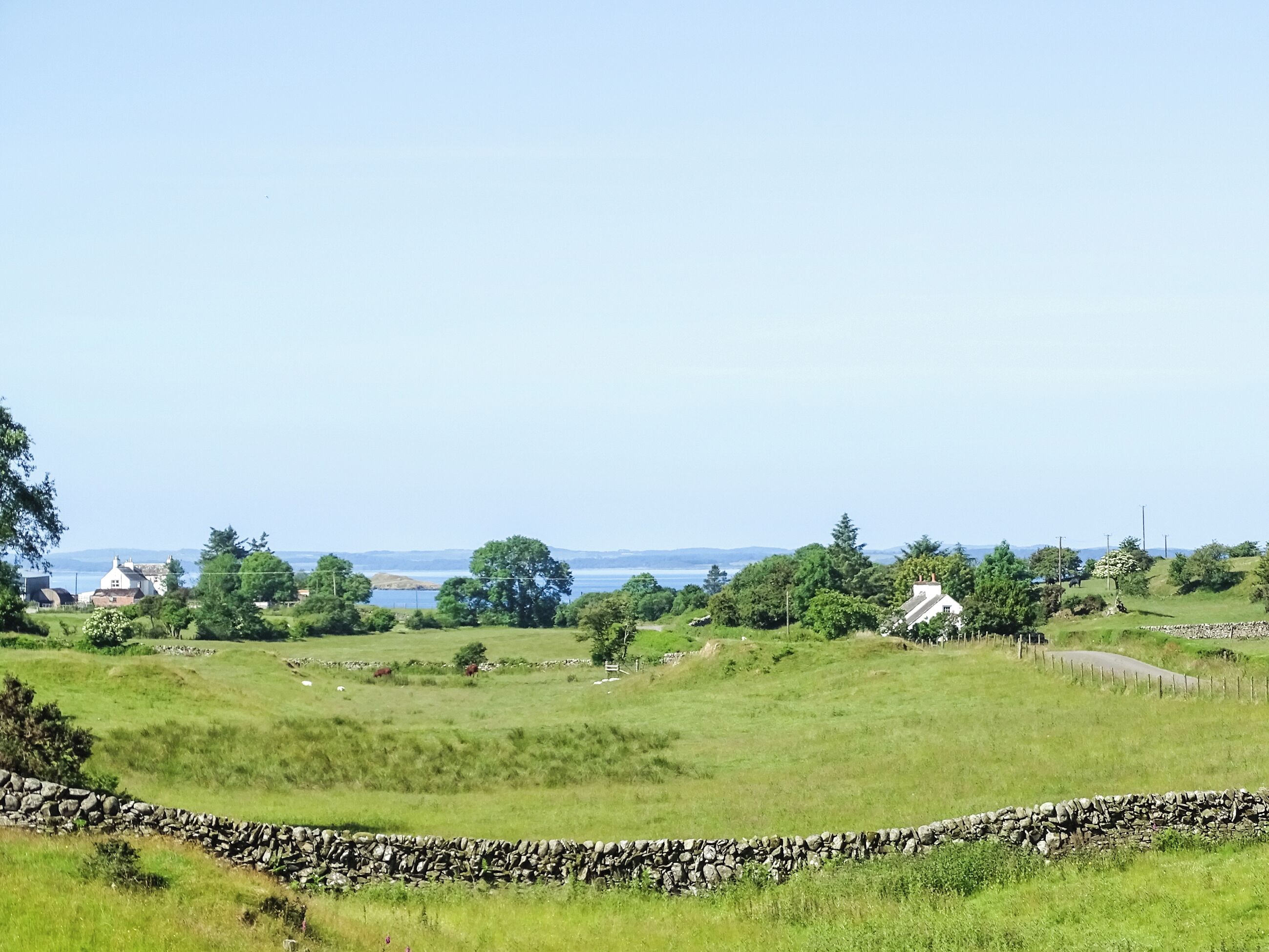 A rural landscape with stone walls, grassy fields, and scattered houses.