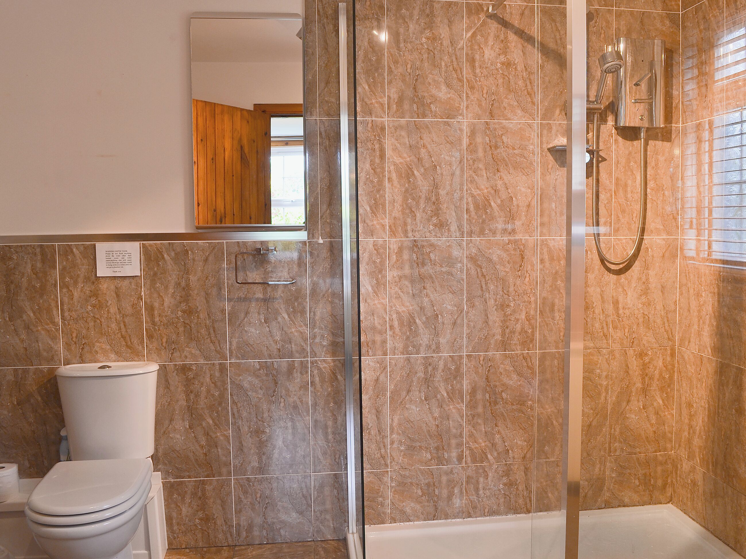 A bathroom with a glass-enclosed shower, a toilet, and a mirror above the sink.