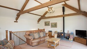 A living room with a brown leather sofa, wooden coffee table, and a fireplace with a black stove. - 3 bedroom accommodation in Alwington, near Bideford (Alwington, near Bideford)