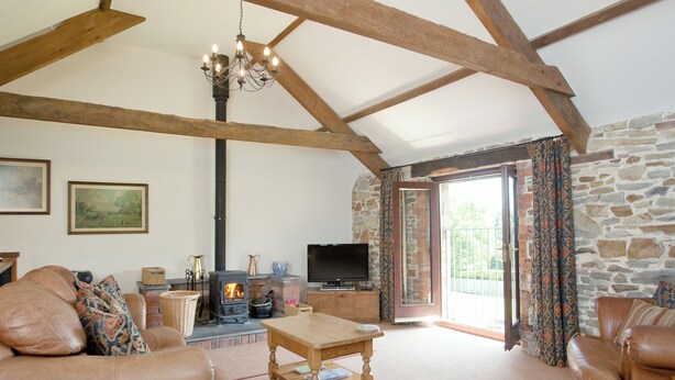 A cozy living room with leather sofas, a wooden table, a fireplace, a television, and a stone wall. - 3 bedroom accommodation in Alwington, near Bideford (Alwington, near Bideford)