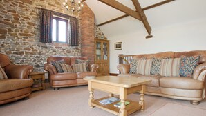 A cozy living room with stone walls, wooden beams, leather sofas, and a wooden coffee table. - 3 bedroom accommodation in Alwington, near Bideford (Alwington, near Bideford)