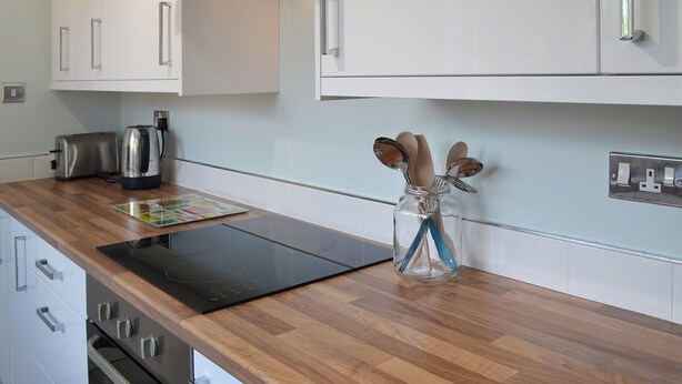 Una cucina moderna con mobili bianchi, un piano di lavoro in legno, un tostapane, un bollitore e un barattolo di vetro con utensili.