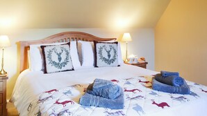 A neatly made bed with a deer print duvet, two decorative pillows, and a bedside table with a lamp and a croissant. - 2 bedroom accommodation in Urray, near Dingwall (Urray, near Dingwall)