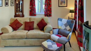 A living room with a sofa, armchair, and curtains. - 3 bedroom accommodation in Bamburgh (Bamburgh)