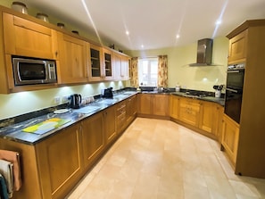 A kitchen with wooden cabinets, a microwave, a stove, and a sink. - 3 bedroom accommodation in Bamburgh (Bamburgh)