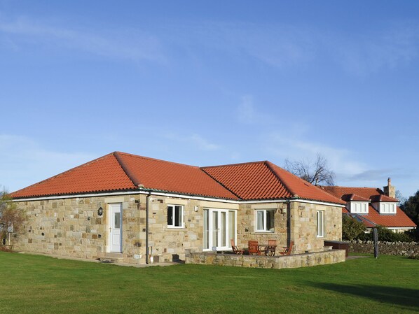A stone building with a red-tiled roof, a front door, and a small porch with chairs. - 3 bedroom accommodation in Bamburgh (Bamburgh)
