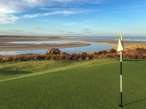 A golf course with a flagstick, water bodies, and a clear sky.