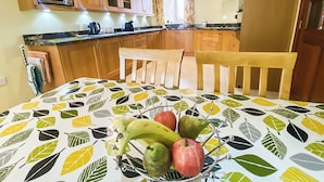 A kitchen with wooden cabinets, a microwave, a dining table with a fruit bowl, and a window with curtains. - 3 bedroom accommodation in Bamburgh (Bamburgh)