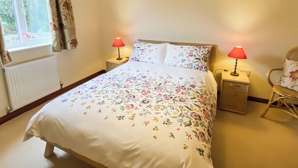 A bedroom with a bed, two bedside lamps, a chair, a window with curtains, and a radiator.