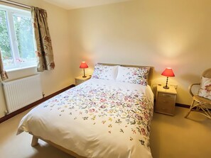 A bedroom with a bed, two bedside lamps, a chair, a window with curtains, and a radiator. - 3 bedroom accommodation in Bamburgh (Bamburgh)