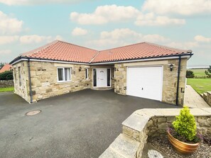 A stone house with a tiled roof, a garage, and a small garden with a potted plant. - 3 bedroom accommodation in Bamburgh (Bamburgh)