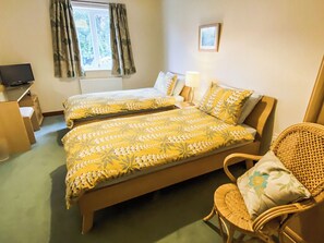 A hotel room with two beds, a chair, a desk, and a television.
