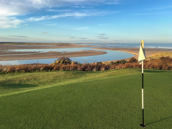 A golf course with a flagstick, water bodies, and a clear sky. - 3 bedroom accommodation in Bamburgh (Bamburgh)