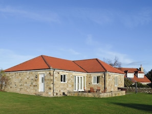 A stone building with a red-tiled roof, a front door, and a small porch with chairs. - 3 bedroom accommodation in Bamburgh (Bamburgh)