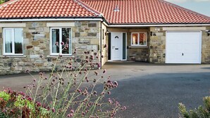 A stone house with a red-tiled roof, a garage, and a driveway. - 3 bedroom accommodation in Bamburgh (Bamburgh)