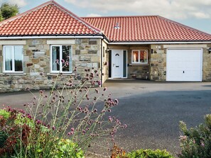 A stone house with a red-tiled roof, a garage, and a driveway.