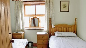A bedroom with two single beds, a wooden headboard, a bedside table with a lamp, a mirror, and a framed picture on the wall. - 3 bedroom accommodation in Crackenthorpe, Appleby (Crackenthorpe, Appleby)