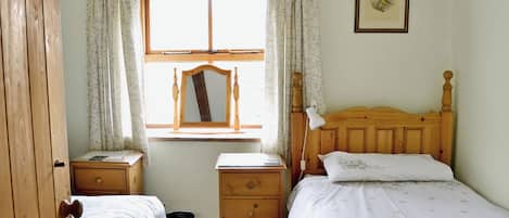 Une chambre à coucher avec deux lits en bois, une commode en bois, une table de chevet, une fenêtre avec un miroir et un tableau encadré au mur.