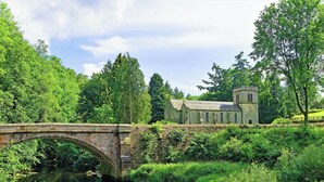 A stone bridge over a river, surrounded by lush greenery and a historic building with a tower. - 3 bedroom accommodation in Crackenthorpe, Appleby (Crackenthorpe, Appleby)