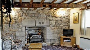 A stone fireplace with a television on a wooden stand, a patterned carpet, and traditional furniture. - 3 bedroom accommodation in Crackenthorpe, Appleby (Crackenthorpe, Appleby)