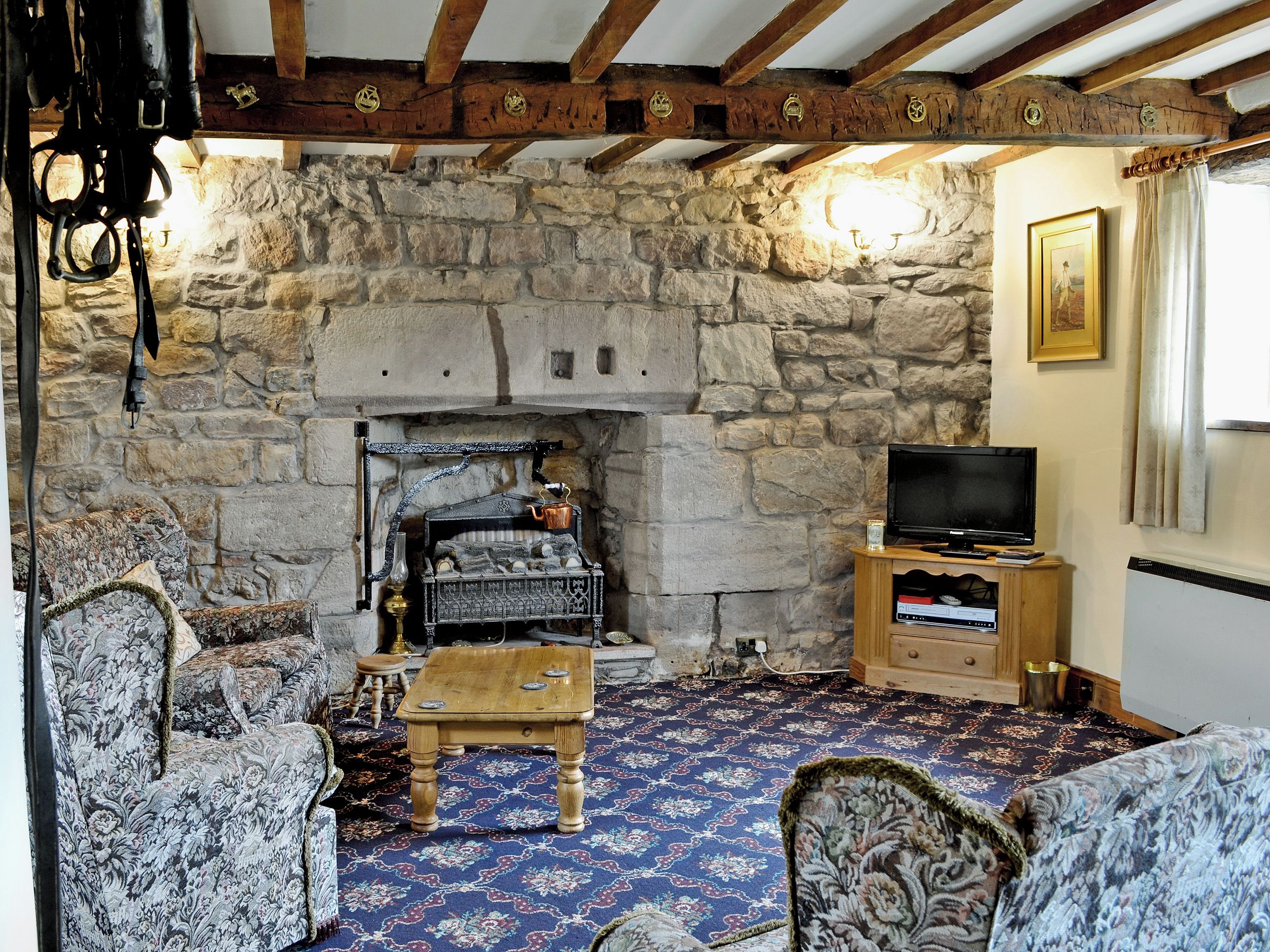 A stone fireplace with a television on a wooden stand, a patterned carpet, and a rustic wooden ceiling.