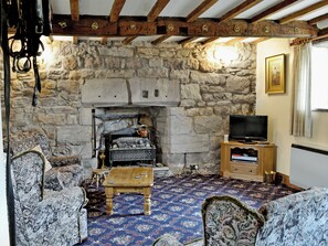 A stone fireplace with a television on a wooden stand, a patterned carpet, and a rustic wooden ceiling.