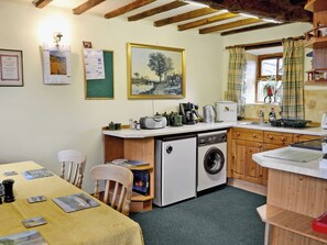 A compact kitchen with a washing machine, a coffee maker, and a dining area with a table set for two.