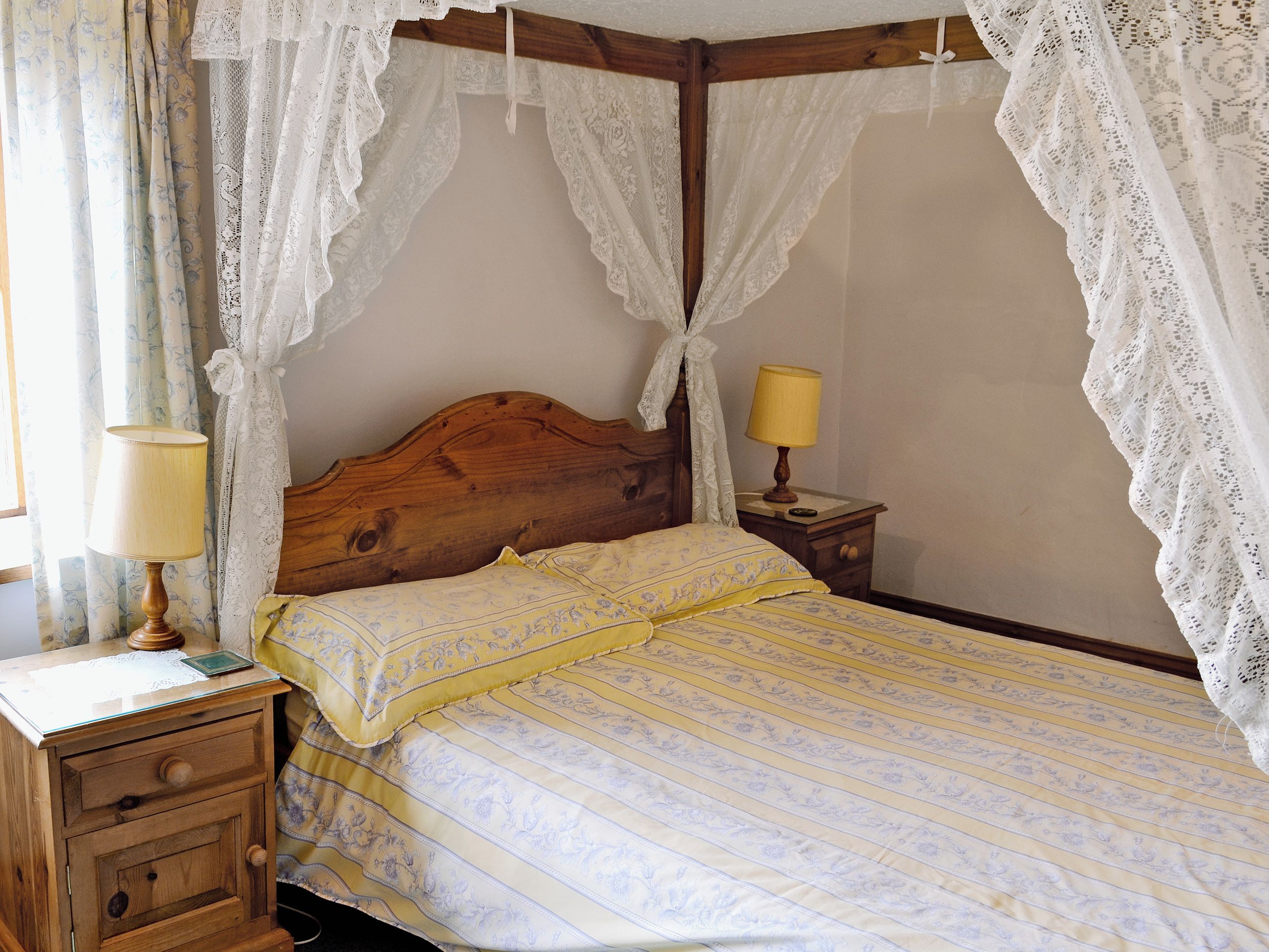 A bedroom with a wooden headboard, a canopy bed, two bedside tables with lamps, and a nightstand with a lamp.