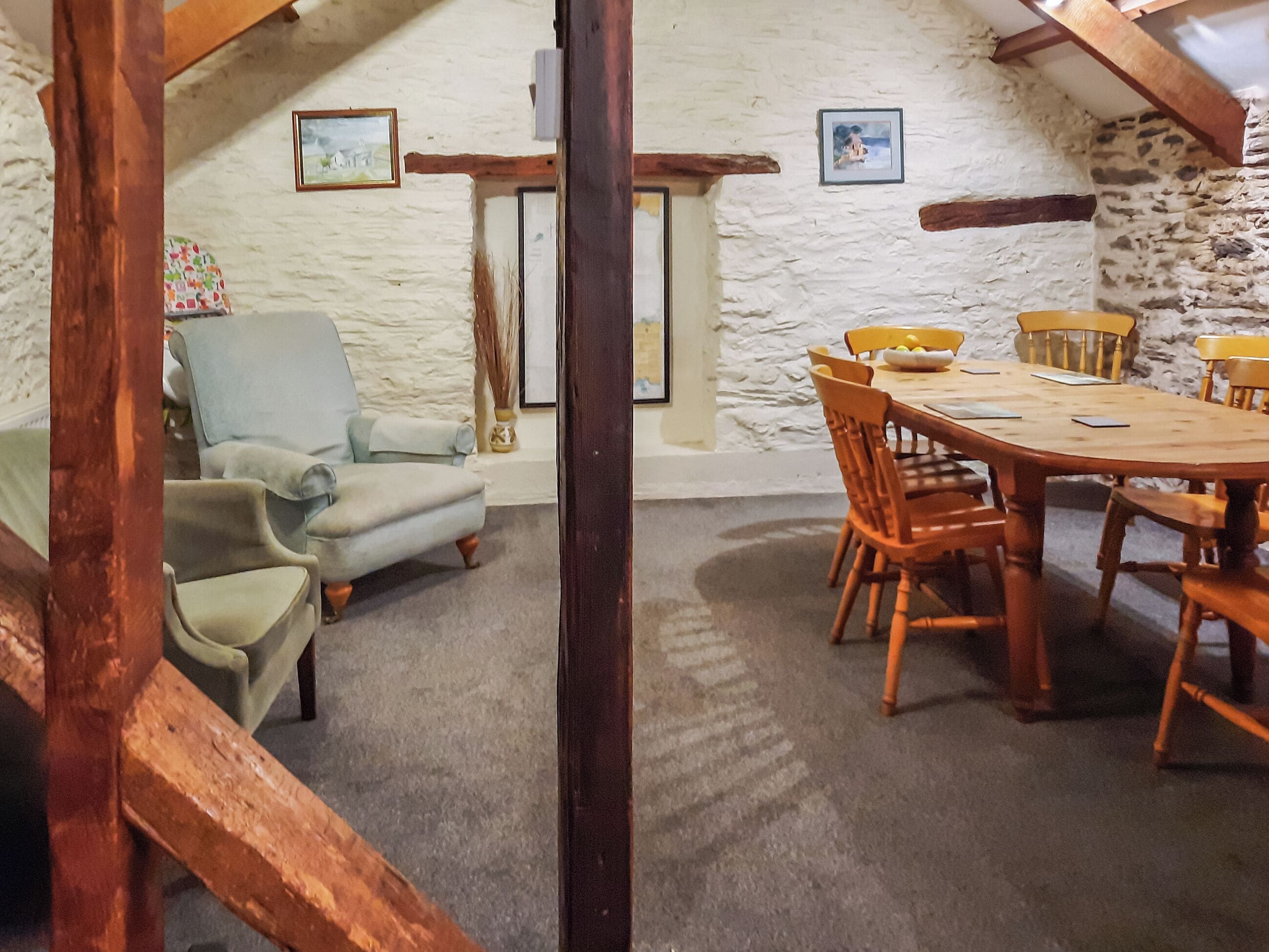 A cozy dining area with a round wooden table and chairs, a light blue armchair, and a stone wall with framed pictures.