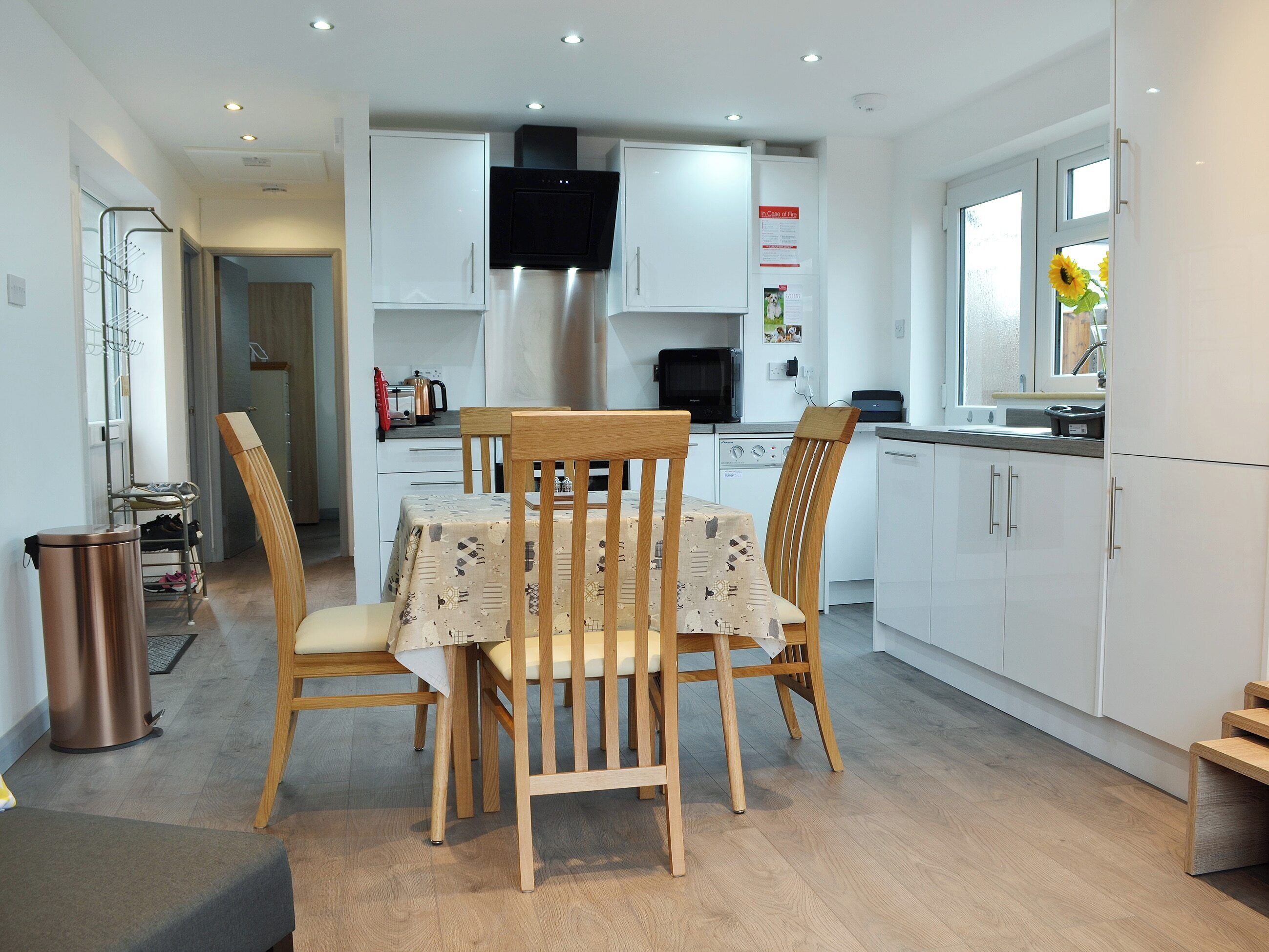 A modern kitchen with white cabinets, a stainless steel range hood, and a dining area with wooden chairs and a table.