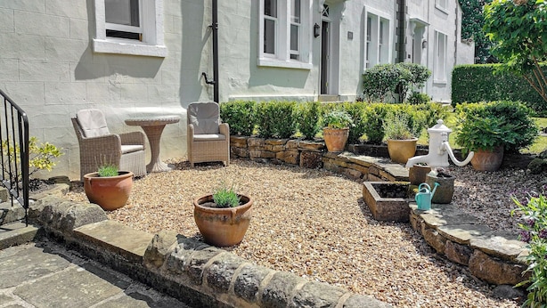 A courtyard with a stone pathway, potted plants, outdoor furniture, and a building with large windows. - 1 bedroom accommodation in Giggleswick, near Settle (Giggleswick, near Settle)