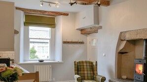 A cozy kitchen with a window, a plaid armchair, a dining table with chairs, and a wood-burning stove. - 1 bedroom accommodation in Giggleswick, near Settle (Giggleswick, near Settle)