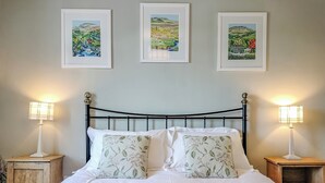 A neatly made bed with white linens and floral pillows, flanked by two bedside tables with lamps, and three framed landscape paintings on the wall above. - 1 bedroom accommodation in Giggleswick, near Settle (Giggleswick, near Settle)