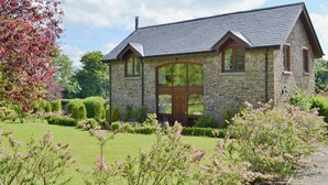 Une maison en pierre avec un toit à deux versants, de grandes fenêtres et un jardin bien entretenu.