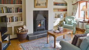 Un salon chaleureux avec une cheminée, des étagères à livres, un téléviseur et des fauteuils confortables.